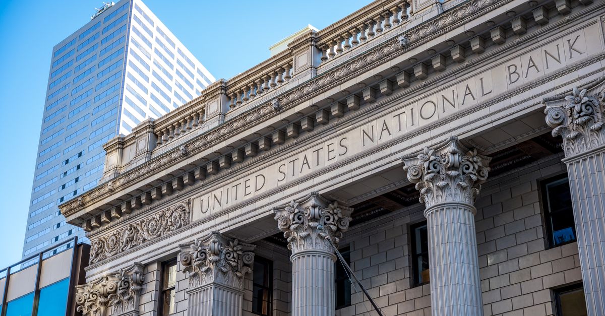 Exterior of historic national bank with decorative elements on classic columns located in city with modern building against blue sky